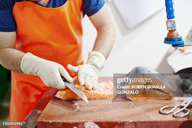 fishmonger wearing an orange apron filleting a salmon at fish market - creative fishing stock pictures, royalty-free photos & images