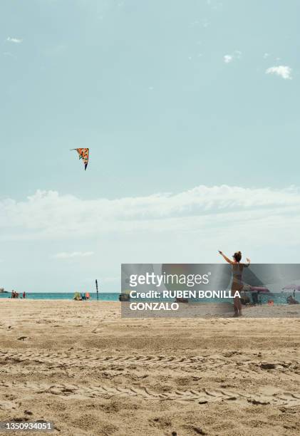 rear view of caucasian teenager girl flying a kite on beach during summer against blue sky - girl blowing sand stock-fotos und bilder