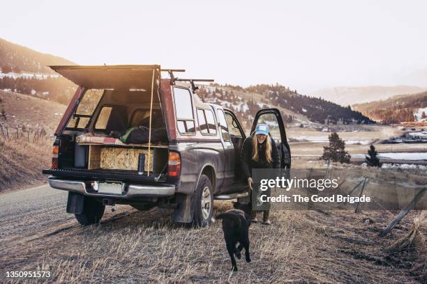 dog running toward young woman on country road during winter - montana western usa stock-fotos und bilder