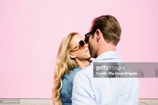 happy couple kissing in front of pink background - kiss stockfoto's en -beelden