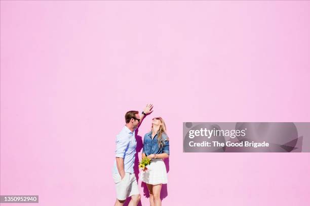 cheerful couple standing against pink background on sunny day - versierd jak stockfoto's en -beelden