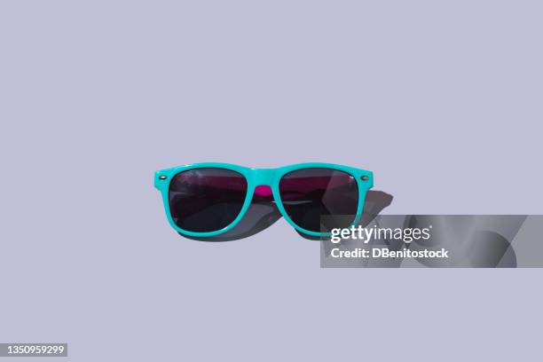 green and fuchsia sunglasses with hard shadow on light blue background. heat, summer and sunlight concept. - sunglasses stock-fotos und bilder