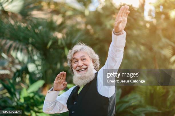 old man, with a big and large beard, making a trap gesture, with a big smile. with a park in the background. old men, beard, bearded, hipster, barber, time, dreams and dates concept. copyspace - big beard stockfoto's en -beelden