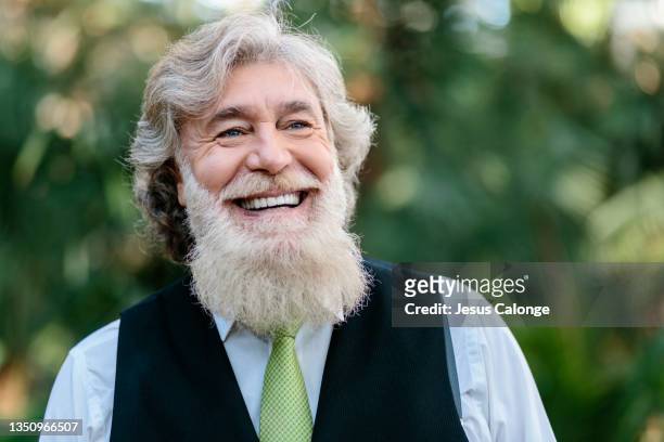 portrait of a old man, with a big and large beard, with a big smile. with a park in the background. old men, beard, bearded, hipster, barber, time, dreams and dates concept. - big beard stockfoto's en -beelden