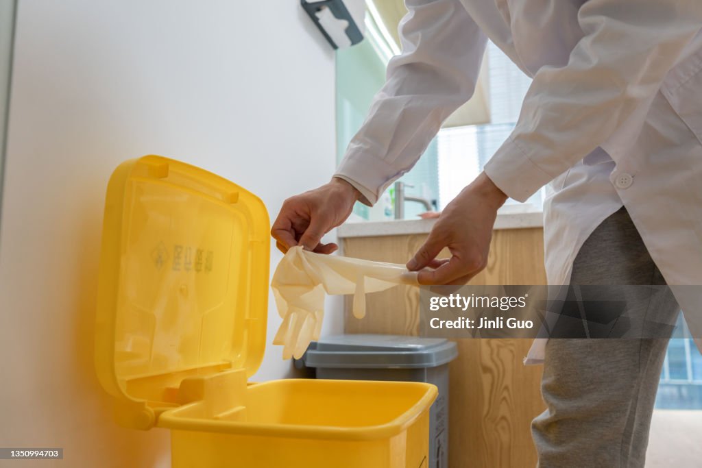 Der Zahnarzt wirft die Einweg-Latexhandschuhe nach der Operation in den entsprechenden Mülleimer