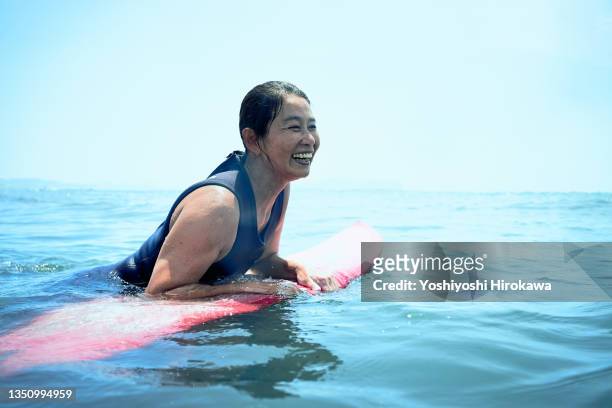 senior woman waiting ocean waves on surfboard - travel experience stock-fotos und bilder