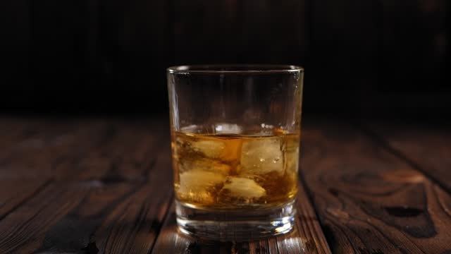Close-up of ice cubes falling into a glass of whiskey on a black background.