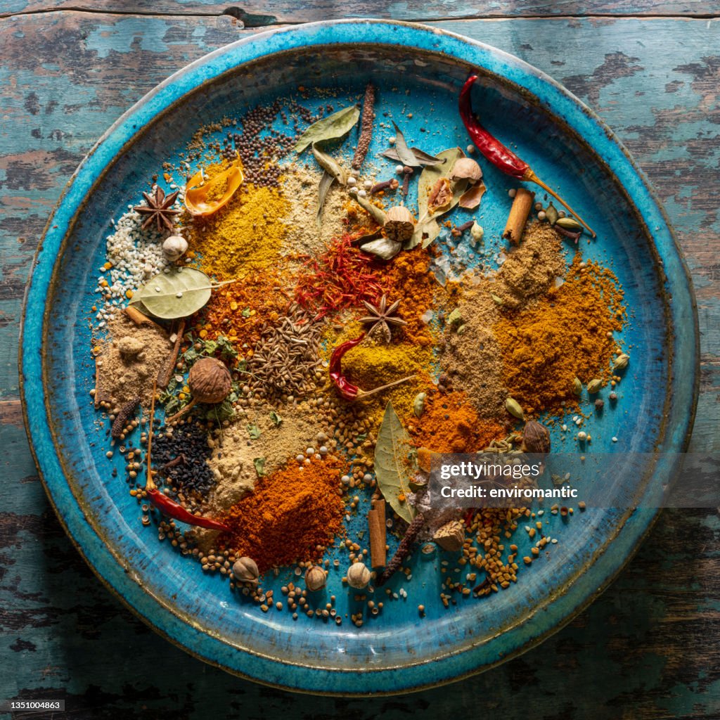 Variety of colorful, organic, dried, vibrant Indian food spices on an old turquoise-colored ceramic plate.