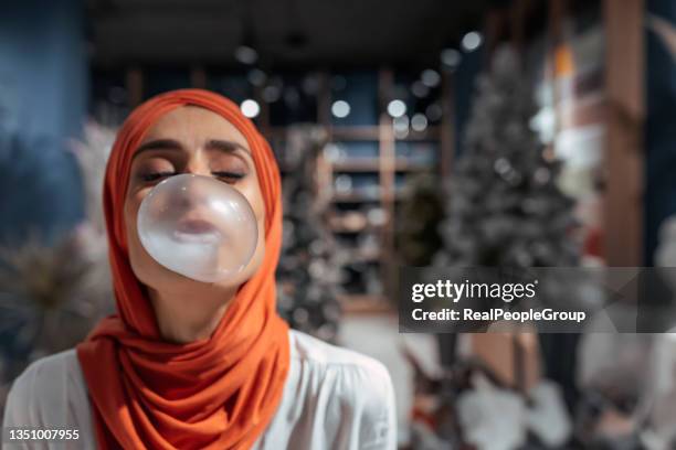 mid adult muslim woman chewing gum and making big balloon - mascar imagens e fotografias de stock