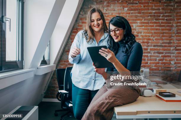 two female co-workers discussing a project idea at the office, using a tablet - heavy set women stock pictures, royalty-free photos & images