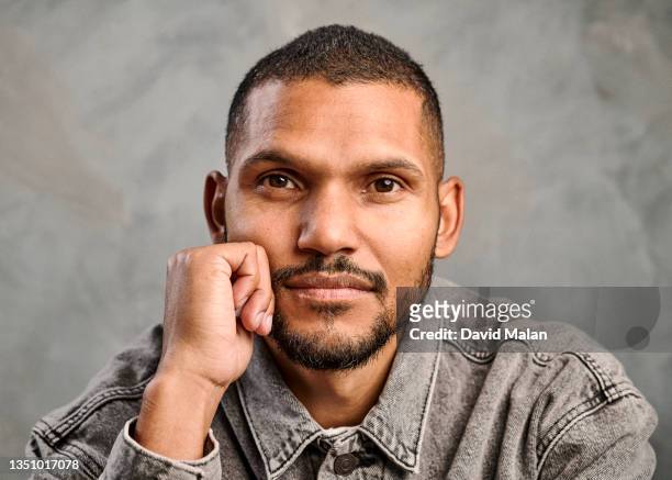 close up studio portrait of a mixed race young man with short dark hair and a beard, wearing a grey denim jacket, looking at camera  with one hand held under his chin. - man looking up beard chin stock-fotos und bilder