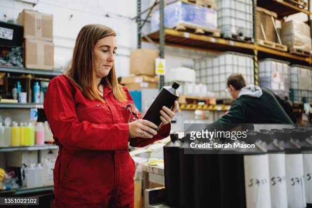 woman in red overalls checking bottles in warehouse - femalefocuscollection stock-fotos und bilder
