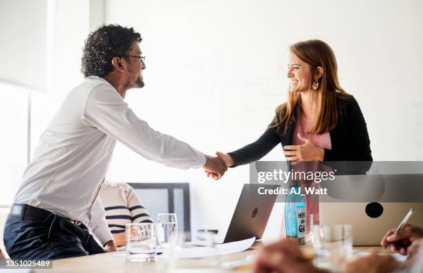 smiling young businesswoman shaking hands with a coworker during a meeting - woman-man-handshake-across-table stock pictures, royalty-free photos & images