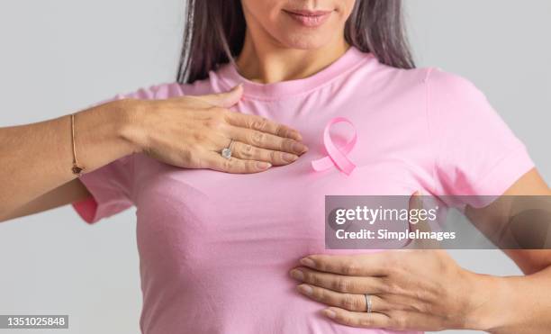 woman in pink shirt and ribbon holds her breast as a symbol of necessity for prevention checks for women. - borstkanker stockfoto's en -beelden