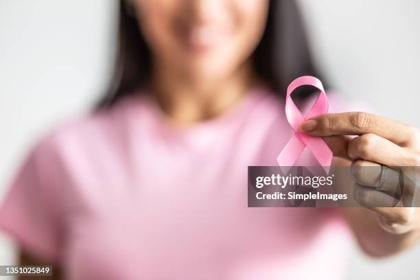 detail of a female hand holding pink ribbon towards the camera to raise breast cancer awareness. - mois photos et images de collection