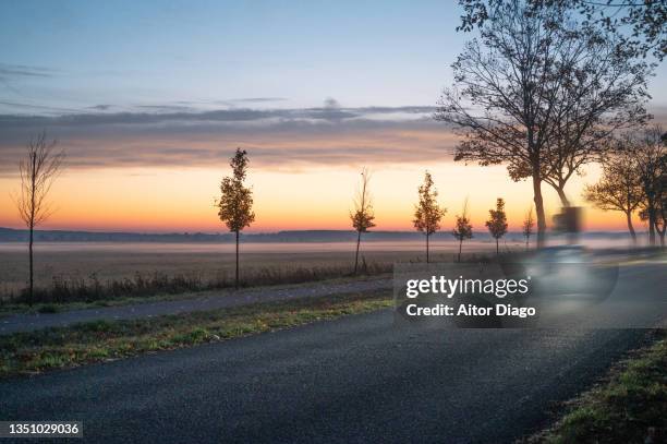 a car drives along a rural road at dawn. germany. - driving in fog stock pictures, royalty-free photos & images