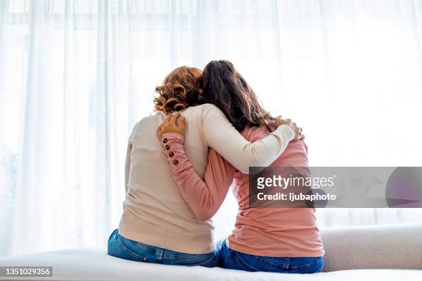 vista trasera de madre e hija abrazando sentadas en la cama - apoyar fotografías e imágenes de stock