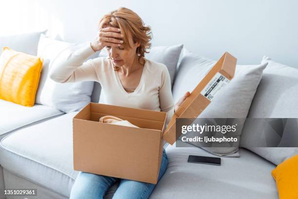 angry shocked young woman unpacking parcel at home - damaged box stock pictures, royalty-free photos & images
