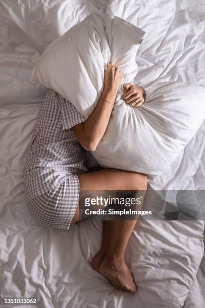 woman in pyjamas holds pillow over her head, trying to cover from light to get more sleep. - bed sleep stockfoto's en -beelden