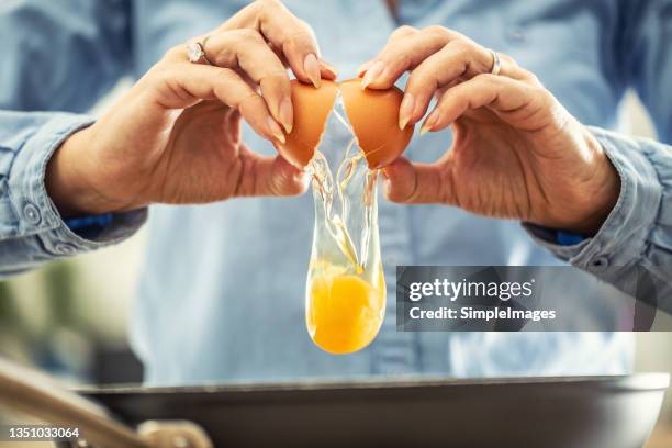 a detail of cracked egg falling into the pan as woman holds egg shells in both hands. - gema de ovo imagens e fotografias de stock