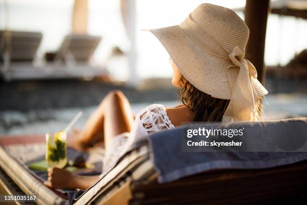 vista trasera de una mujer despreocupada en una tumbona en la playa. - silla de playa fotografías e imágenes de stock