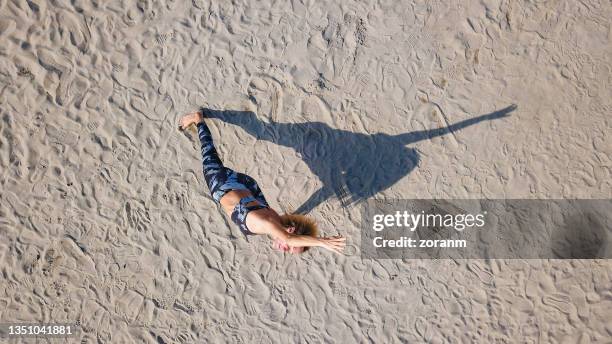 Drone view on woman in Extended side angle pose, casting shadow on sand ...