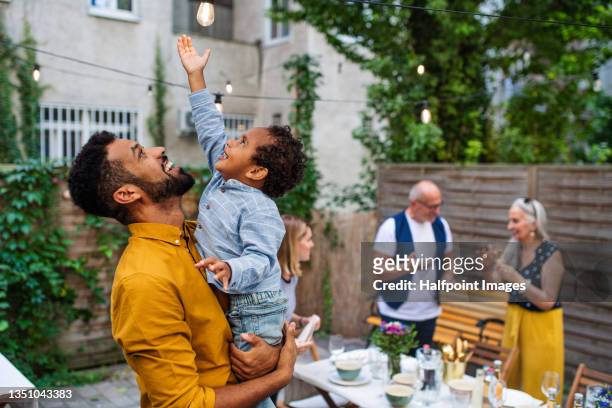 happy father holding his small son pointing to light bulb during family dinner outdoors in garden. - summer lights stockfoto's en -beelden