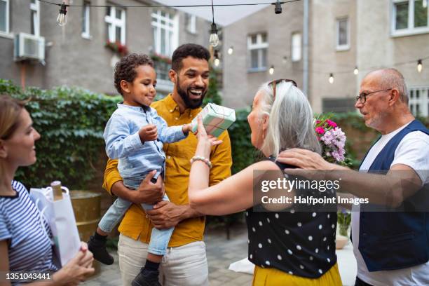 little multiracial boy with parents congratulating his grandmother outdoors in garden. - diverse family stock-fotos und bilder