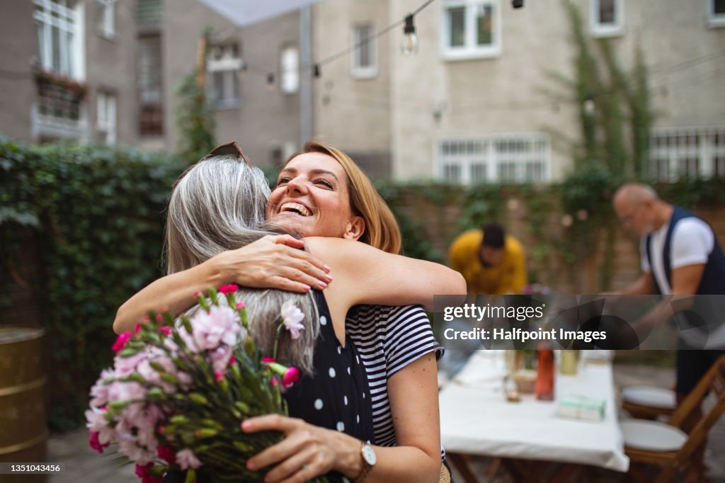 Happy adult daughter with bouquet hugging her senior mother outdoors in garden.