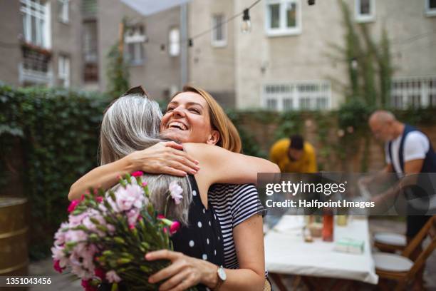 happy adult daughter with bouquet hugging her senior mother outdoors in garden. - fête des mères photos et images de collection
