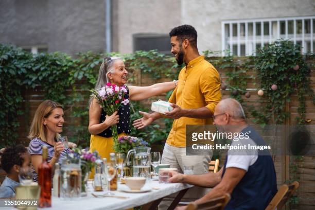 happy young man with bouquet and gift congratulating his senior mother in law outdoors in garden. - mother in law ストックフォトと画像