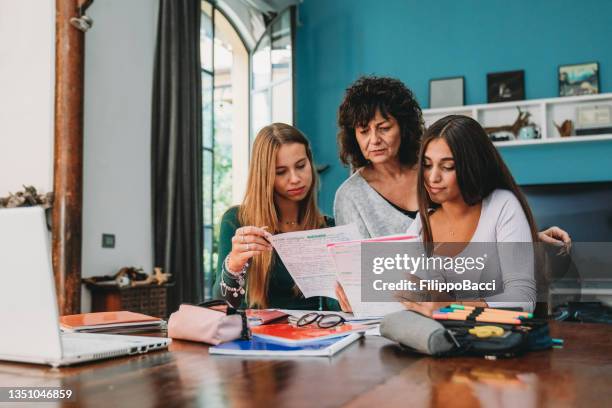 a mother is helping her daughter and a friend with the homework - laatstejaars high school stockfoto's en -beelden