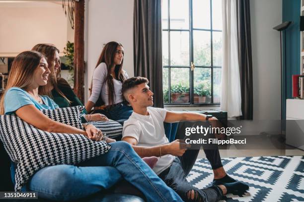 quatre amis qui regardent la télévision à la maison - étudiant canapé photos et images de collection