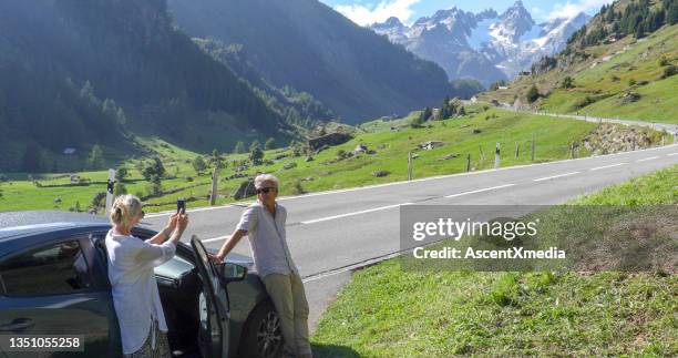 pareja madura se relaja fuera del coche, disfrutando del aire fresco alpino - roadside memorial fotografías e imágenes de stock