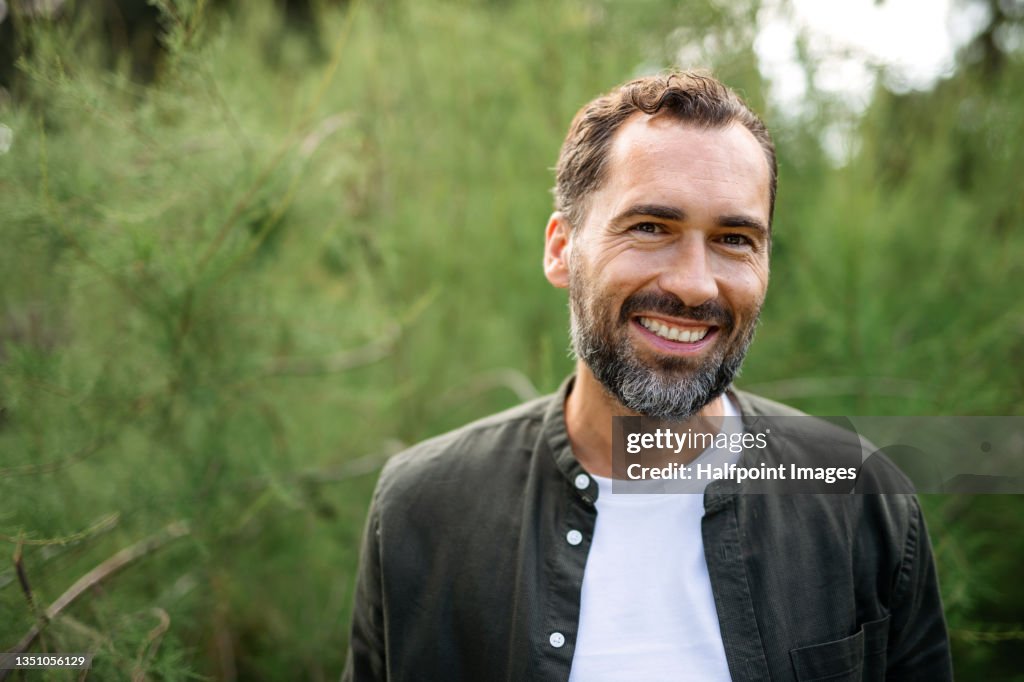 Portrait of happy mature man resting outdoors in park, looking at camera.