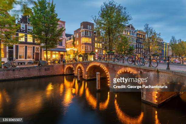 illuminated bridge in amsterdam, the netherlands at dusk - amsterdam stock pictures, royalty-free photos & images