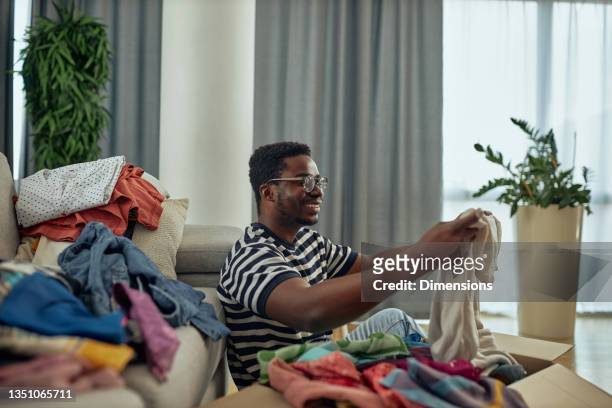 young man putting clothes into a donation box at home - coat check stock pictures, royalty-free photos & images