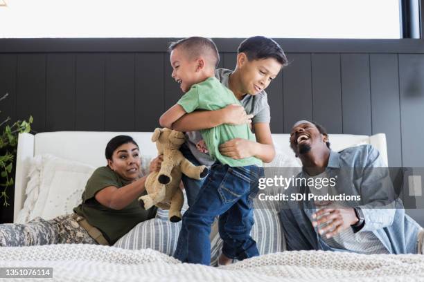 dad laughs and mom worries as sons wrestle on bed - rough housing stock pictures, royalty-free photos & images