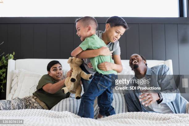 dad laughs and mom worries as sons wrestle on bed - 玩耍式打鬧 個照片及圖片檔