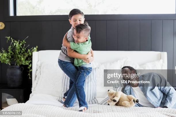 single dad smiles as sons wrestle on bed - mixed wrestling imagens e fotografias de stock