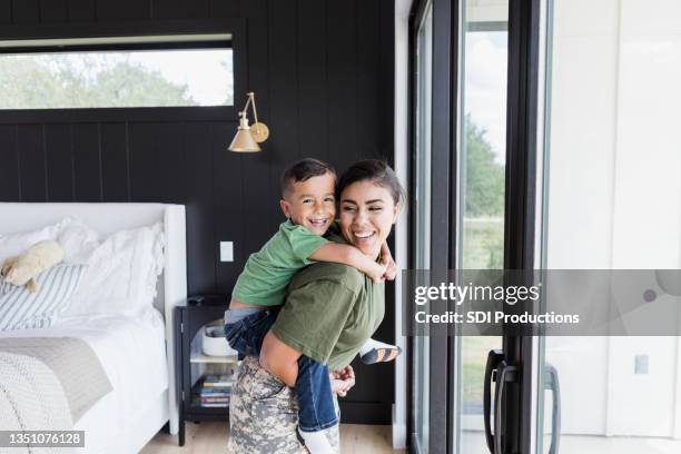 soldier mom gives son piggy back ride near sliding doors - sliding door stock pictures, royalty-free photos & images