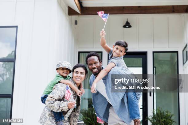 dad and soldier wife give sons piggy back rides - family smiling at front door stock pictures, royalty-free photos & images