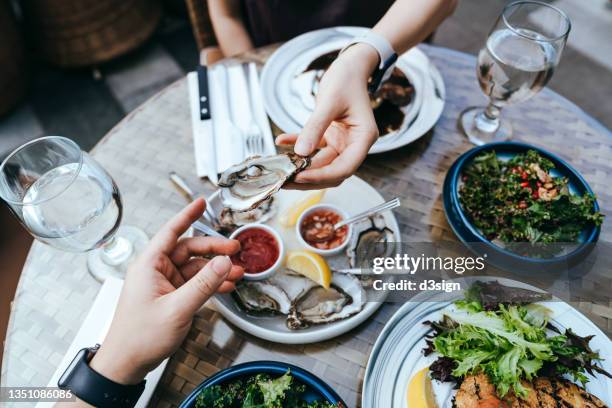 high angle view of woman passing fresh oyster to man across the dining table during lunch, enjoying a scrumptious meal in outdoor restaurant. sharing and togetherness. eating out lifestyle. outdoor dining concept - ostron bildbanksfoton och bilder