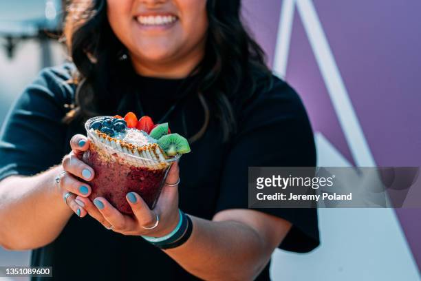 cheerful young latina woman holding a healthy acai food bowl outside a food truck - acai berries stockfoto's en -beelden
