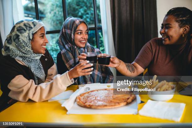 three friends are toasting with cola during a pizza dinner - moroccan girl stock pictures, royalty-free photos & images