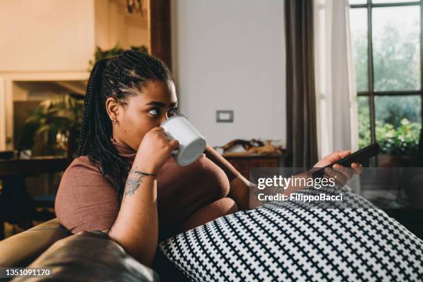 mujer mestiza está viendo la televisión y tomando un café en el sofá - servicio a la carta fotografías e imágenes de stock