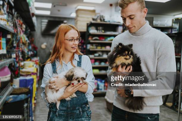 happy couple buying toys and food for their dog in pet shop. - pet shop stock pictures, royalty-free photos & images