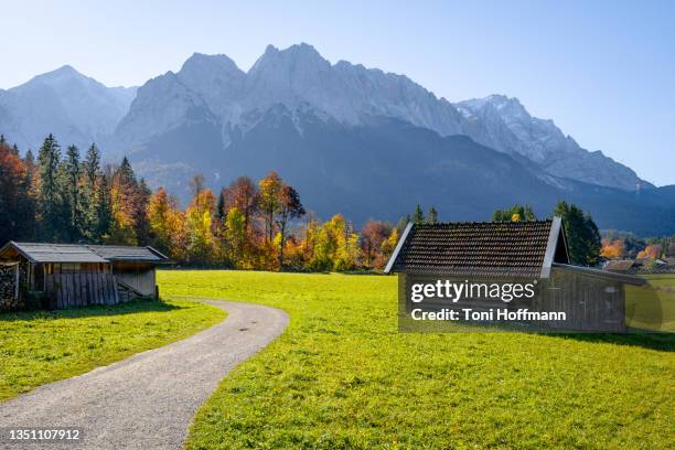 hiking path leading through bavarian cabins with zugspitze in the background - lake riegsee stock pictures, royalty-free photos & images