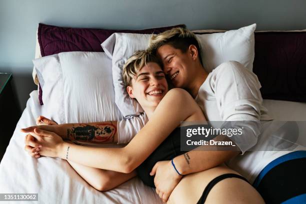 lesbian couple at home, waking up together in bed and kissing - lesbian bed stock pictures, royalty-free photos & images