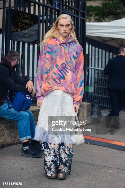 Model Angel wears a Collina Strada multicolor "Collina Land" quilted round hem hoodie, white lace dress, over blue floral pants, boots, and a small...